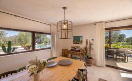 Bright and airy dining area featuring a wooden table, stylish pendant light, and large windows overlooking a serene outdoor pool and garden. The space is decorated with natural elements and a cozy aesthetic, perfect for entertaining.