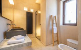 Modern bathroom featuring a minimalist design with a concrete sink, walk-in shower, and natural light from a window. Towel rack and neatly arranged towels enhance the aesthetic appeal.