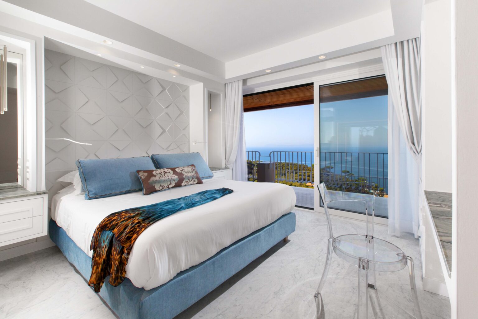 Modern bedroom with a king-sized bed, stylish decor, and large windows offering a stunning ocean view. The room features light-colored walls, elegant furnishings, and a cozy atmosphere, perfect for relaxation. | Only on SopranoVillas