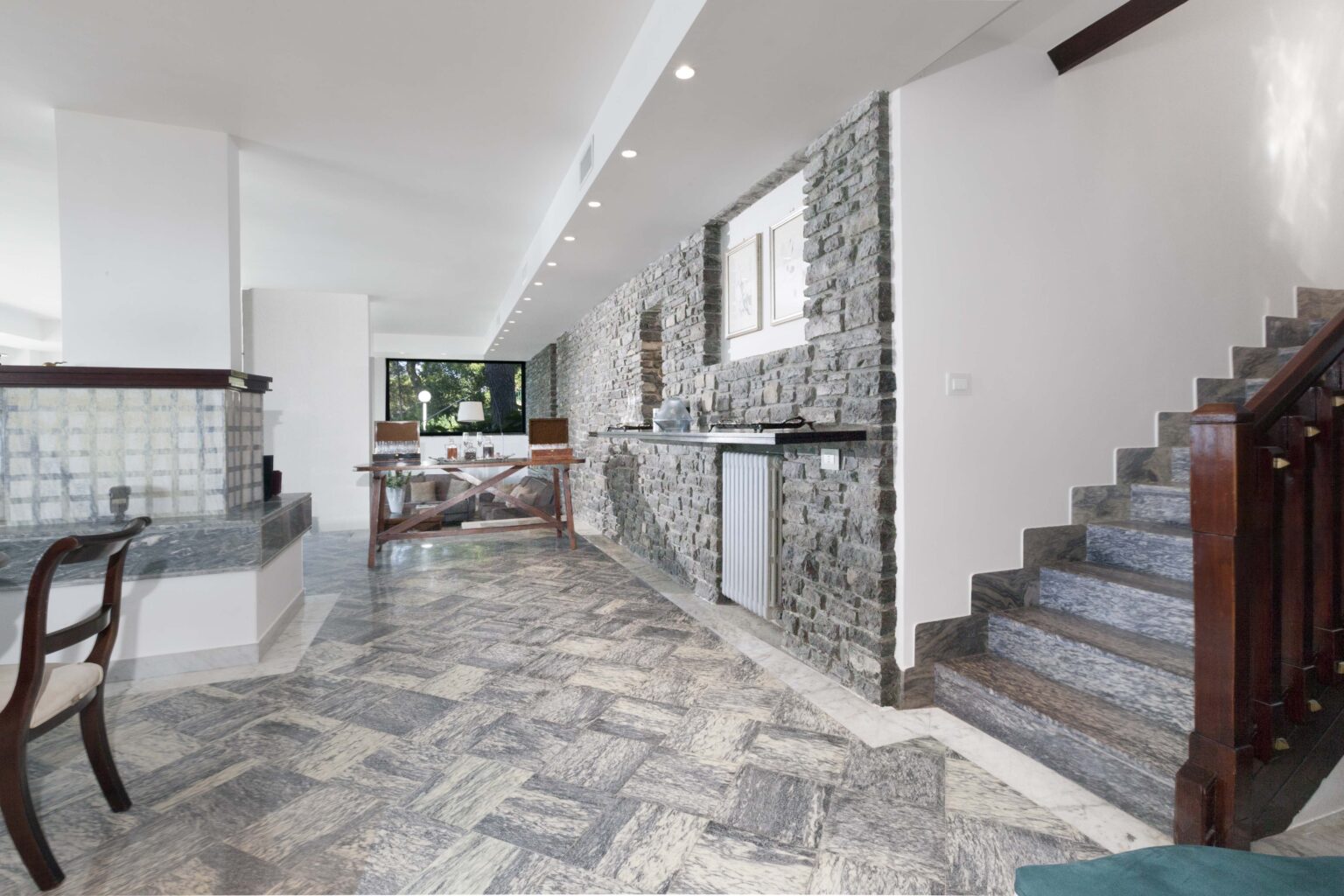 Modern interior of a spacious home featuring stone walls, tiled flooring, and a staircase leading to the upper level, with a view of an open kitchen and dining area. | Only on SopranoVillas