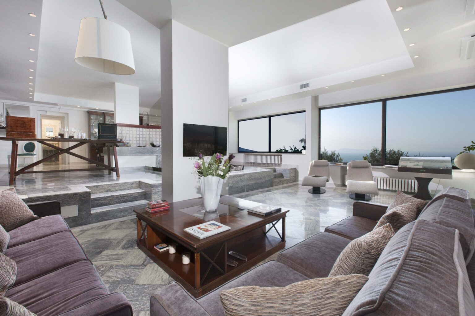 Spacious modern living room featuring large windows with scenic views, elegant furniture, and contemporary decor, perfect for relaxation and entertaining. | Only on SopranoVillas