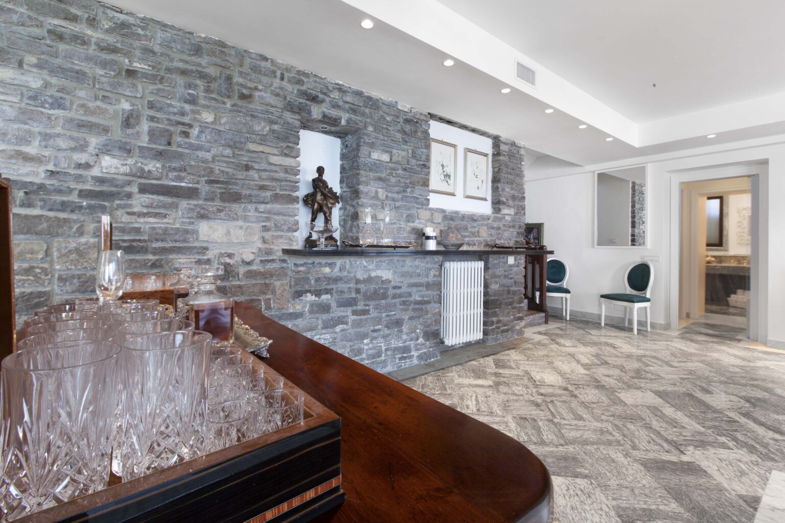 Modern interior design featuring a stylish bar area with a stone accent wall, elegant glassware, and contemporary decor elements, creating a sophisticated atmosphere in a spacious living area. | Only on SopranoVillas
