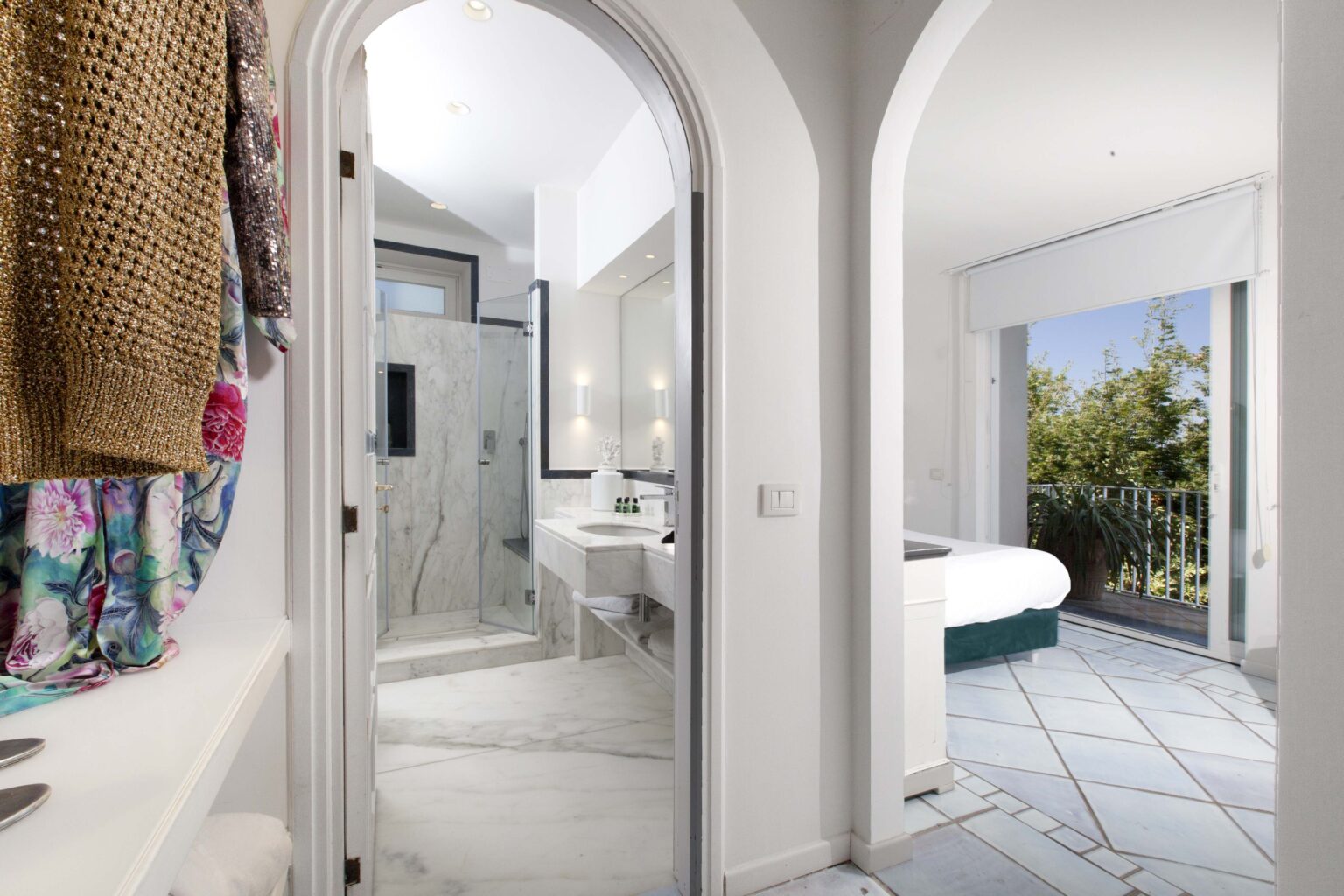 Modern bathroom and bedroom interior featuring marble flooring, a glass shower, and natural light from large windows. The space is elegantly designed with an open layout, showcasing stylish decor and a cozy atmosphere. | Only on SopranoVillas