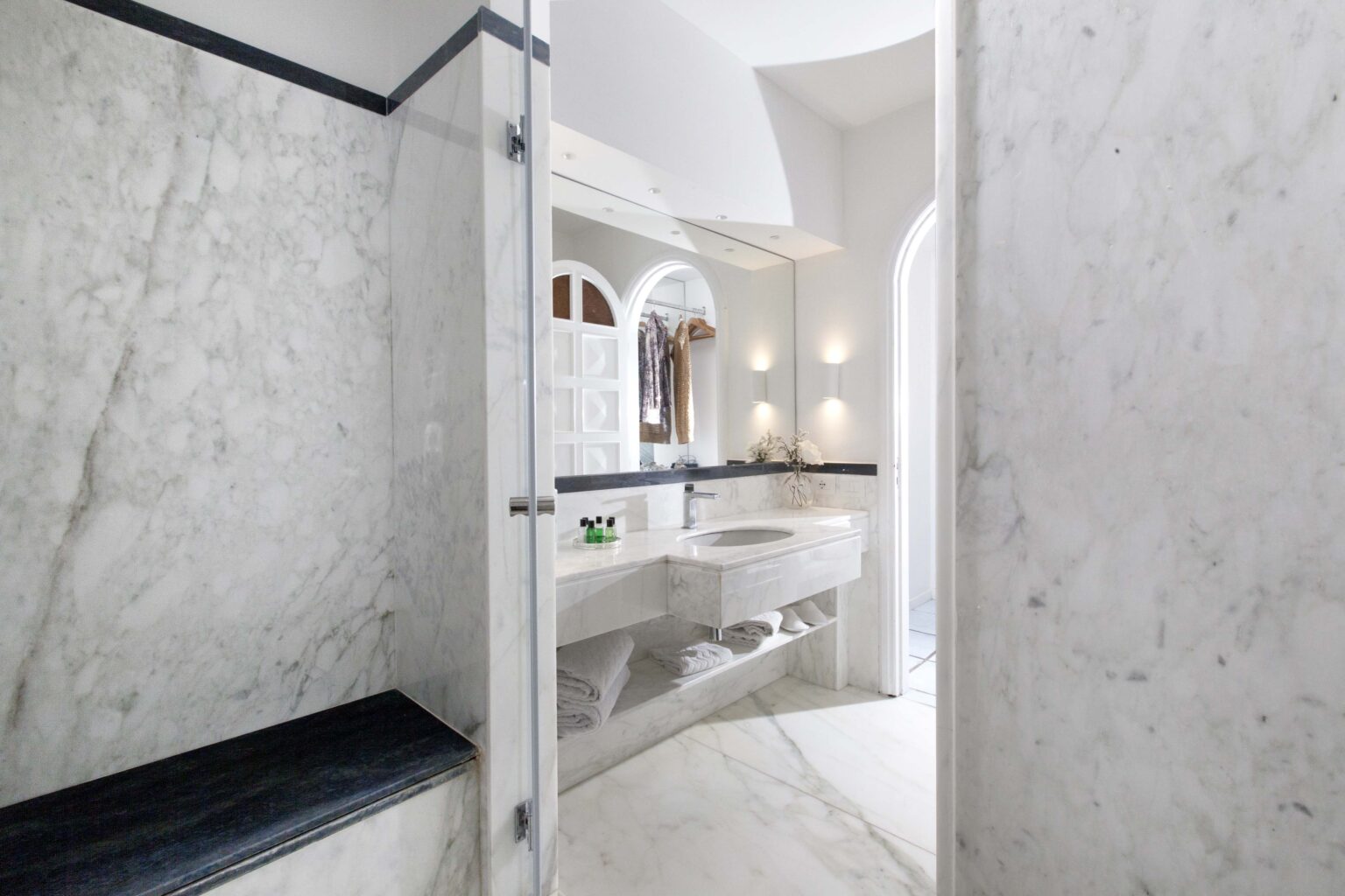 Modern marble bathroom featuring a spacious walk-in shower, elegant sink area, and stylish fixtures, illuminated by soft lighting for a luxurious ambiance. | Only on SopranoVillas