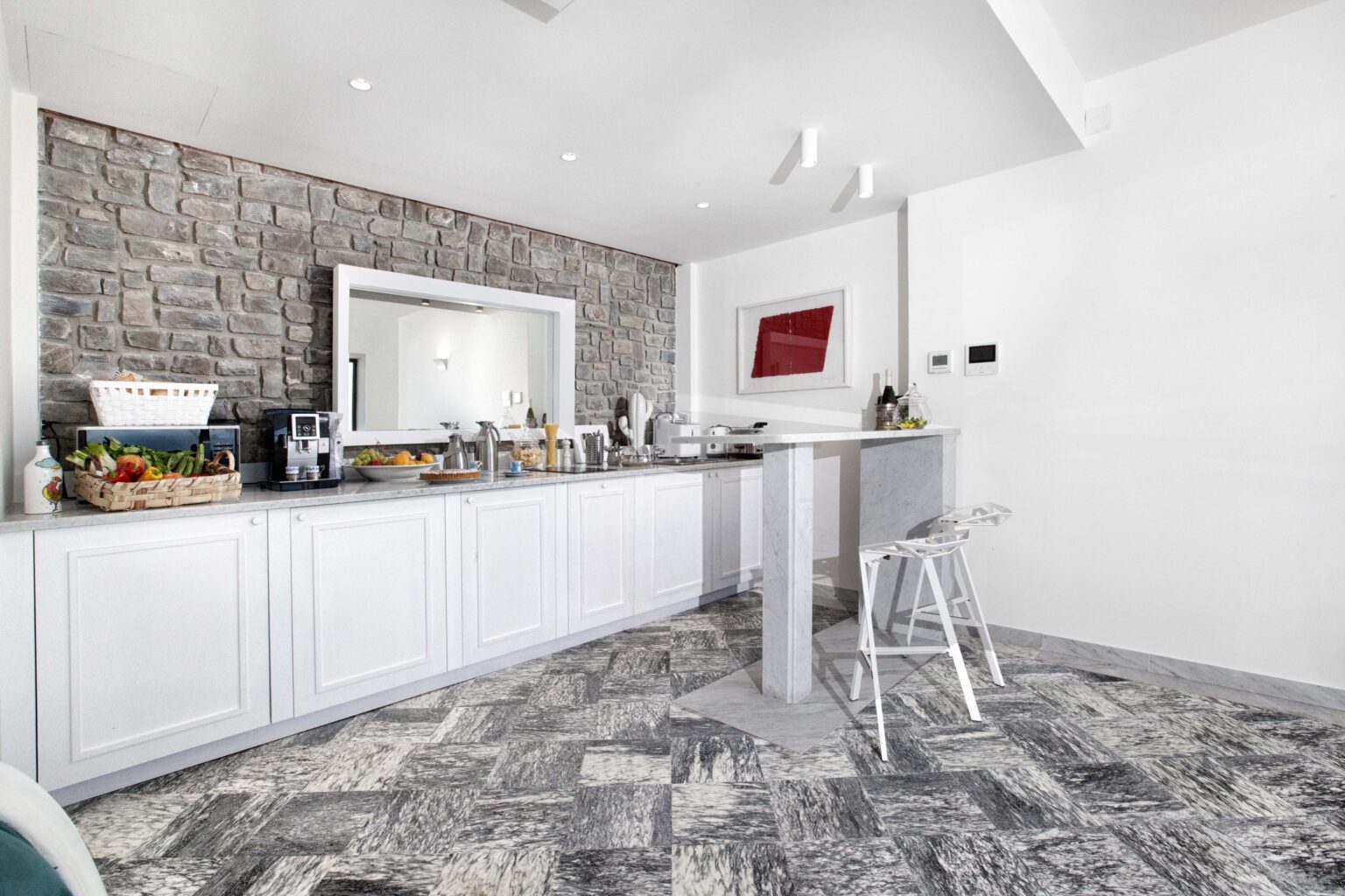 Modern kitchen interior featuring white cabinetry, a stone accent wall, and a stylish bar area with a stool, complemented by a contemporary design and elegant lighting. | Only on SopranoVillas