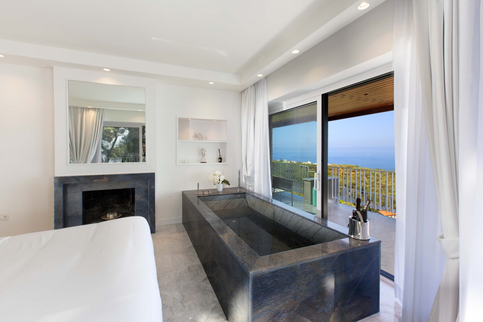 Modern bedroom with a sleek design featuring a luxurious freestanding bathtub, large windows offering a stunning ocean view, and minimalist decor for a serene atmosphere. | Only on SopranoVillas