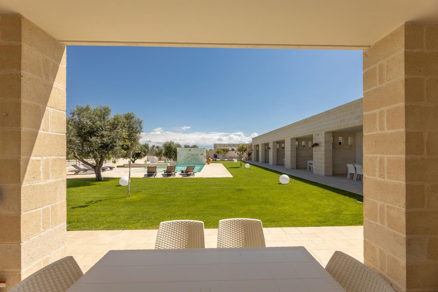 Modern outdoor view from a stone-framed patio, showcasing a lush green lawn, contemporary architecture, and clear blue skies, ideal for relaxation and outdoor gatherings. | Only on SopranoVillas