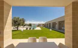 Modern outdoor view from a stone-framed patio, showcasing a lush green lawn, contemporary architecture, and clear blue skies, ideal for relaxation and outdoor gatherings.