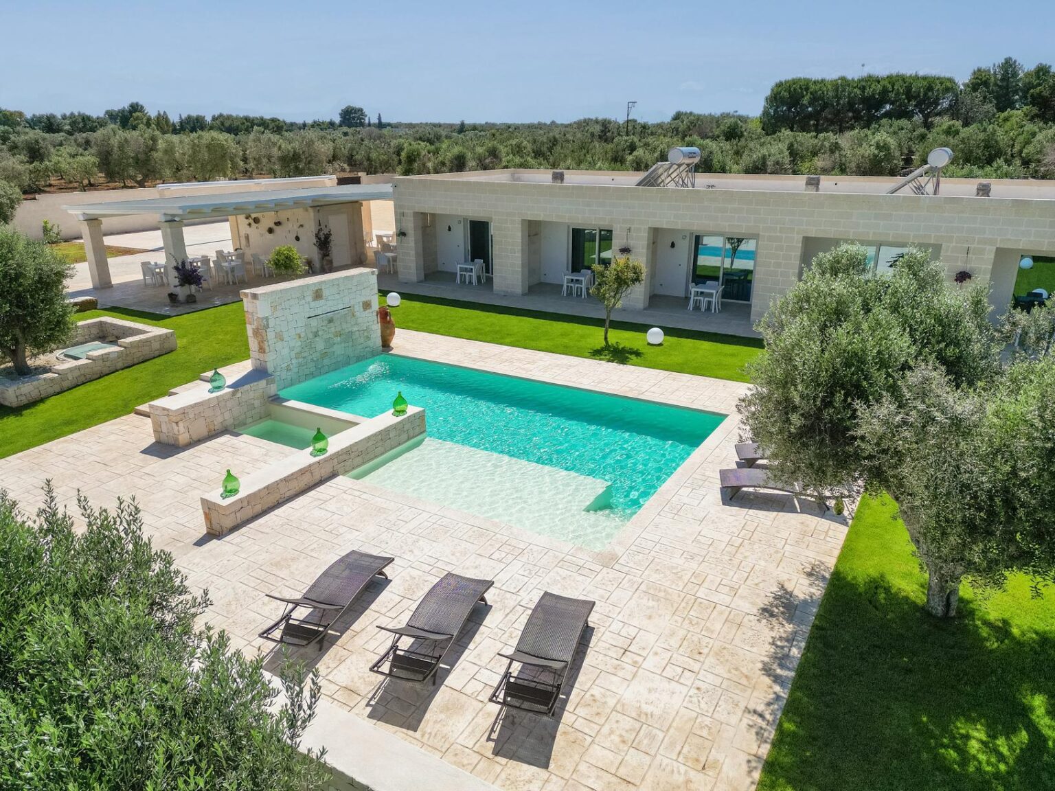 Aerial view of a modern villa with a turquoise swimming pool surrounded by lush greenery, sun loungers, and a serene outdoor space, ideal for relaxation and leisure. | Only on SopranoVillas