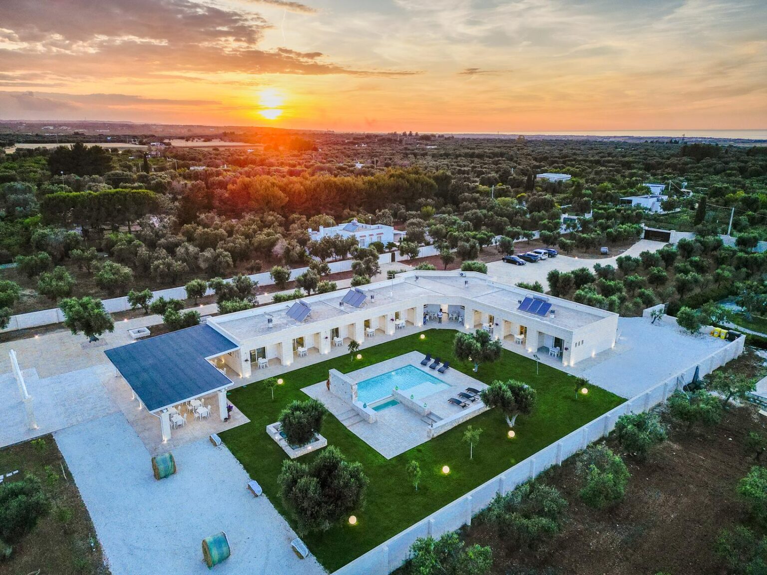 Aerial view of a modern villa with a swimming pool surrounded by lush greenery at sunset, showcasing an inviting outdoor space and serene landscape. | Only on SopranoVillas