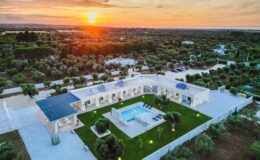 Aerial view of a modern villa with a swimming pool surrounded by lush greenery at sunset, showcasing an inviting outdoor space and serene landscape.