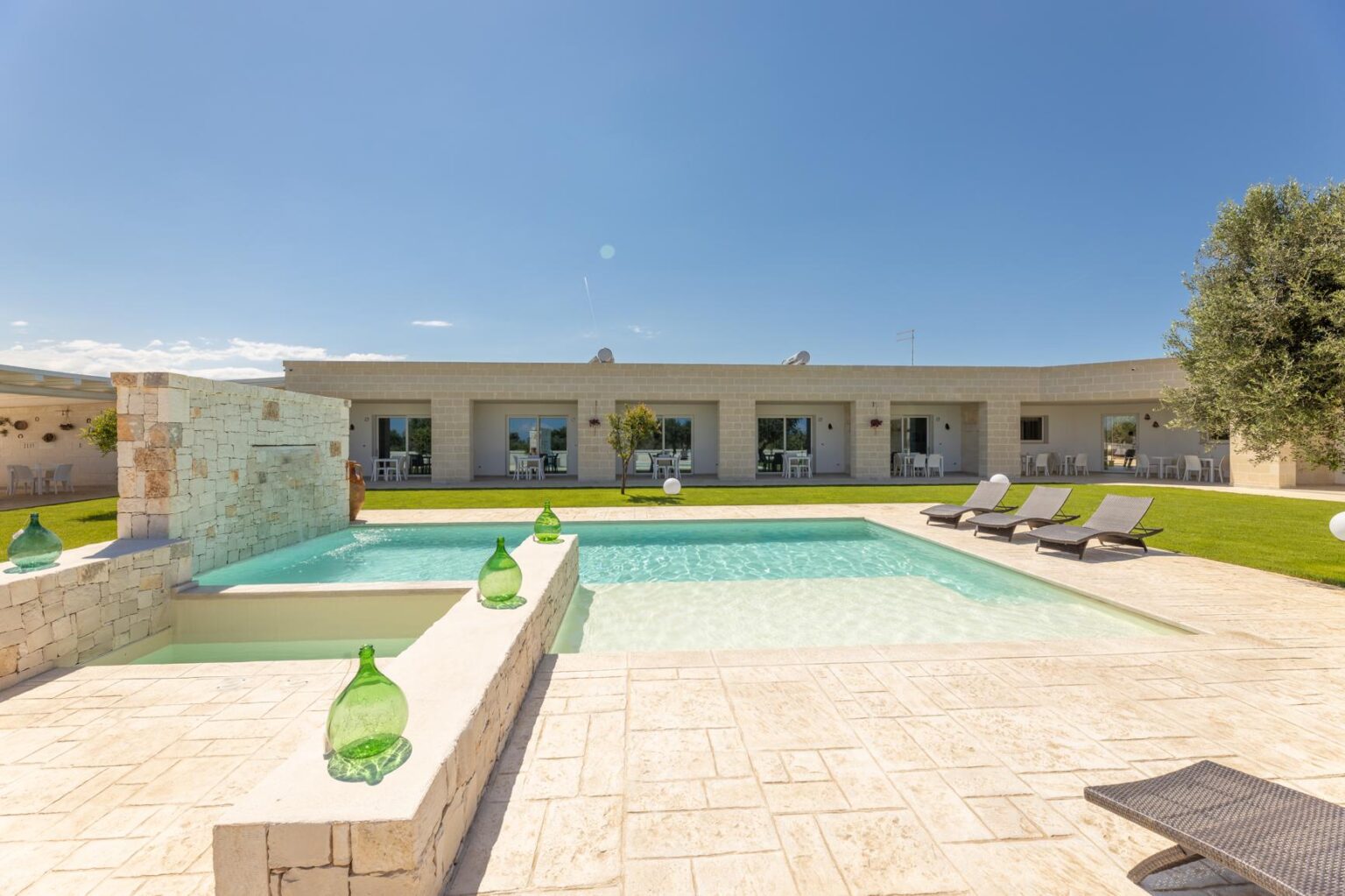 Modern villa with a swimming pool and sun loungers, surrounded by green grass and clear blue sky, ideal for luxury vacation rentals. | Only on SopranoVillas