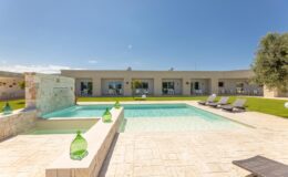Modern villa with a swimming pool and sun loungers, surrounded by green grass and clear blue sky, ideal for luxury vacation rentals.