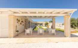 Modern outdoor dining area featuring a covered patio with white chairs and a scenic view of a landscaped garden. Ideal for gatherings and al fresco dining in a sunny environment.