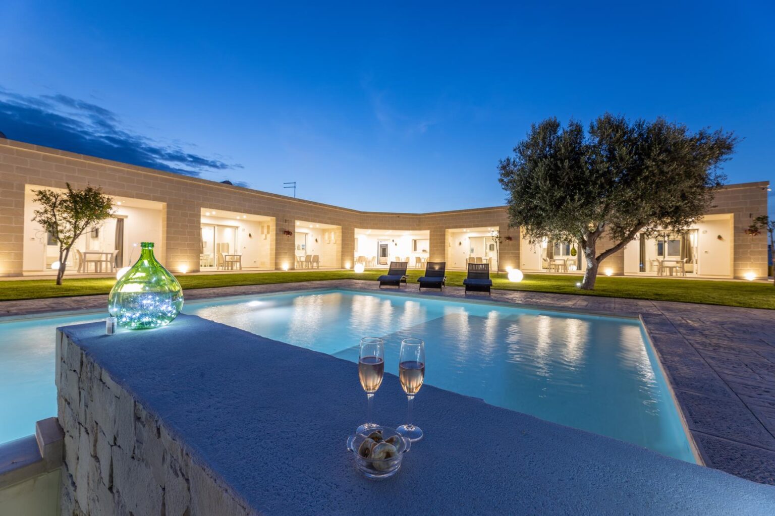 Luxurious villa with a serene swimming pool, surrounded by landscaped gardens and illuminated by soft evening lights, perfect for relaxation and outdoor gatherings. | Only on SopranoVillas