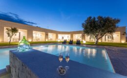 Luxurious villa with a serene swimming pool, surrounded by landscaped gardens and illuminated by soft evening lights, perfect for relaxation and outdoor gatherings.
