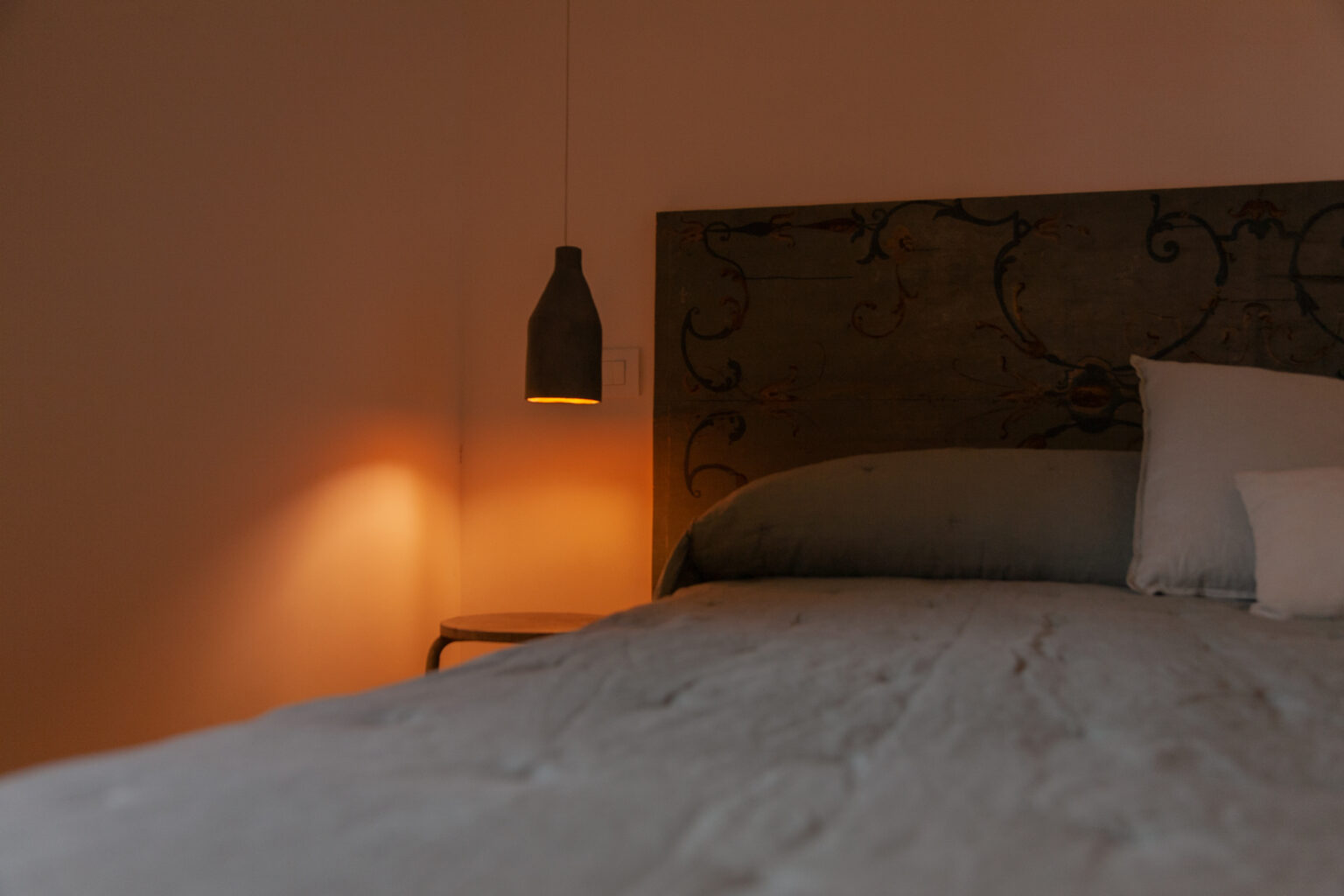 Cozy bedroom featuring a decorative headboard, soft bedding, and a stylish pendant light casting a warm glow on a side table, creating a serene atmosphere. | Only on SopranoVillas