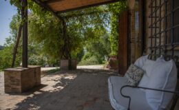 Charming outdoor seating area with a rustic stone floor, shaded by a wooden pergola adorned with lush greenery, offering a peaceful view of the surrounding landscape. Ideal for relaxation and enjoying nature.