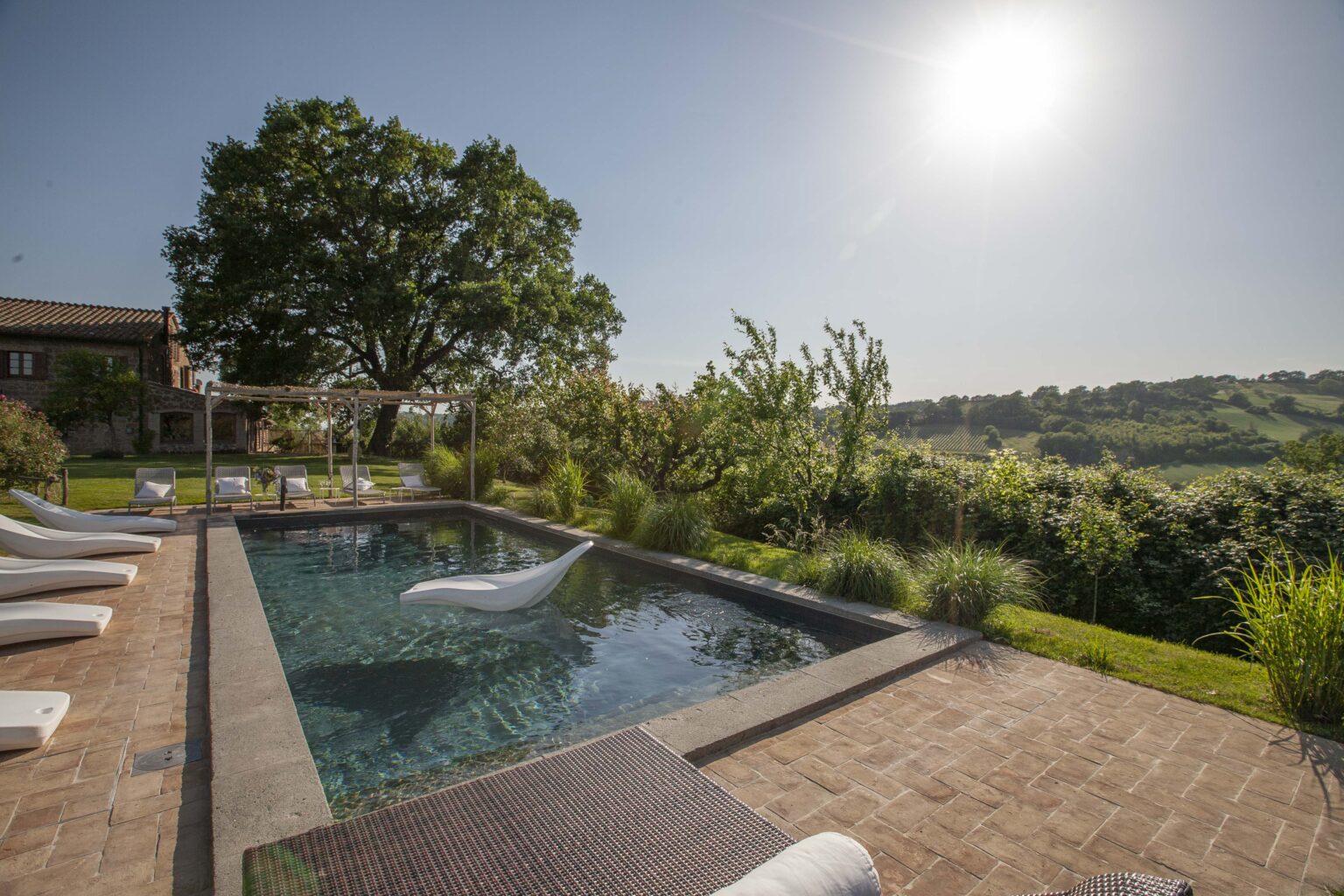 Luxurious outdoor swimming pool surrounded by lush greenery and sun loungers, with a scenic view of rolling hills under a bright sun. Ideal for relaxation and leisure. | Only on SopranoVillas
