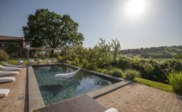 Luxurious outdoor swimming pool surrounded by lush greenery and sun loungers, with a scenic view of rolling hills under a bright sun. Ideal for relaxation and leisure.
