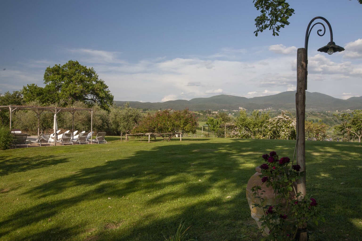 Scenic view of a lush green landscape with a lamp post, featuring rolling hills in the background and a seating area under trees, ideal for outdoor gatherings. | Only on SopranoVillas