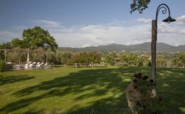 Scenic view of a lush green landscape with a lamp post, featuring rolling hills in the background and a seating area under trees, ideal for outdoor gatherings.