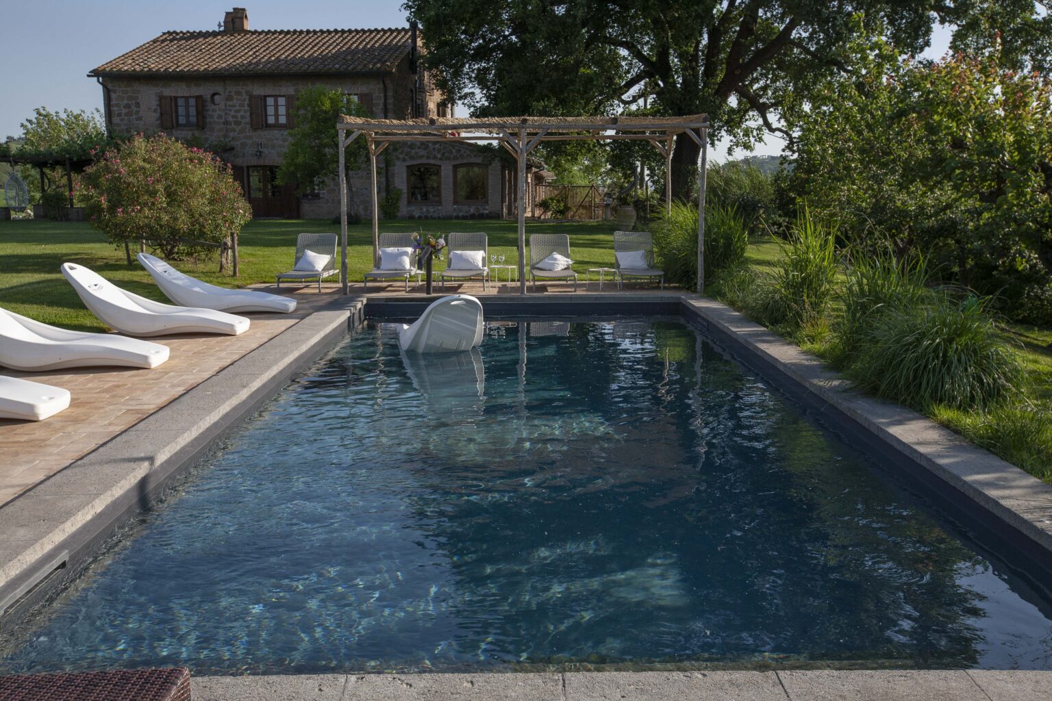 Luxury outdoor swimming pool surrounded by lounge chairs and lush greenery, with a charming house in the background, ideal for relaxation and leisure. | Only on SopranoVillas