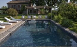 Luxury outdoor swimming pool surrounded by lounge chairs and lush greenery, with a charming house in the background, ideal for relaxation and leisure.