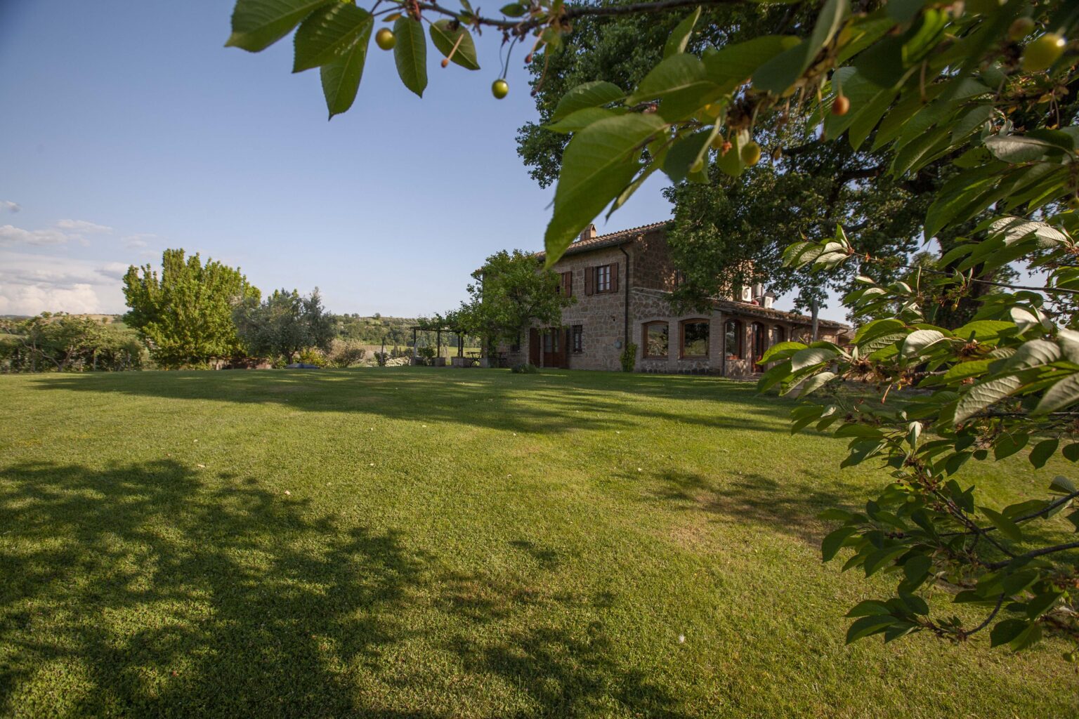 Scenic view of a spacious green lawn with a rustic house surrounded by trees under a clear blue sky, ideal for outdoor relaxation and nature enjoyment. | Only on SopranoVillas