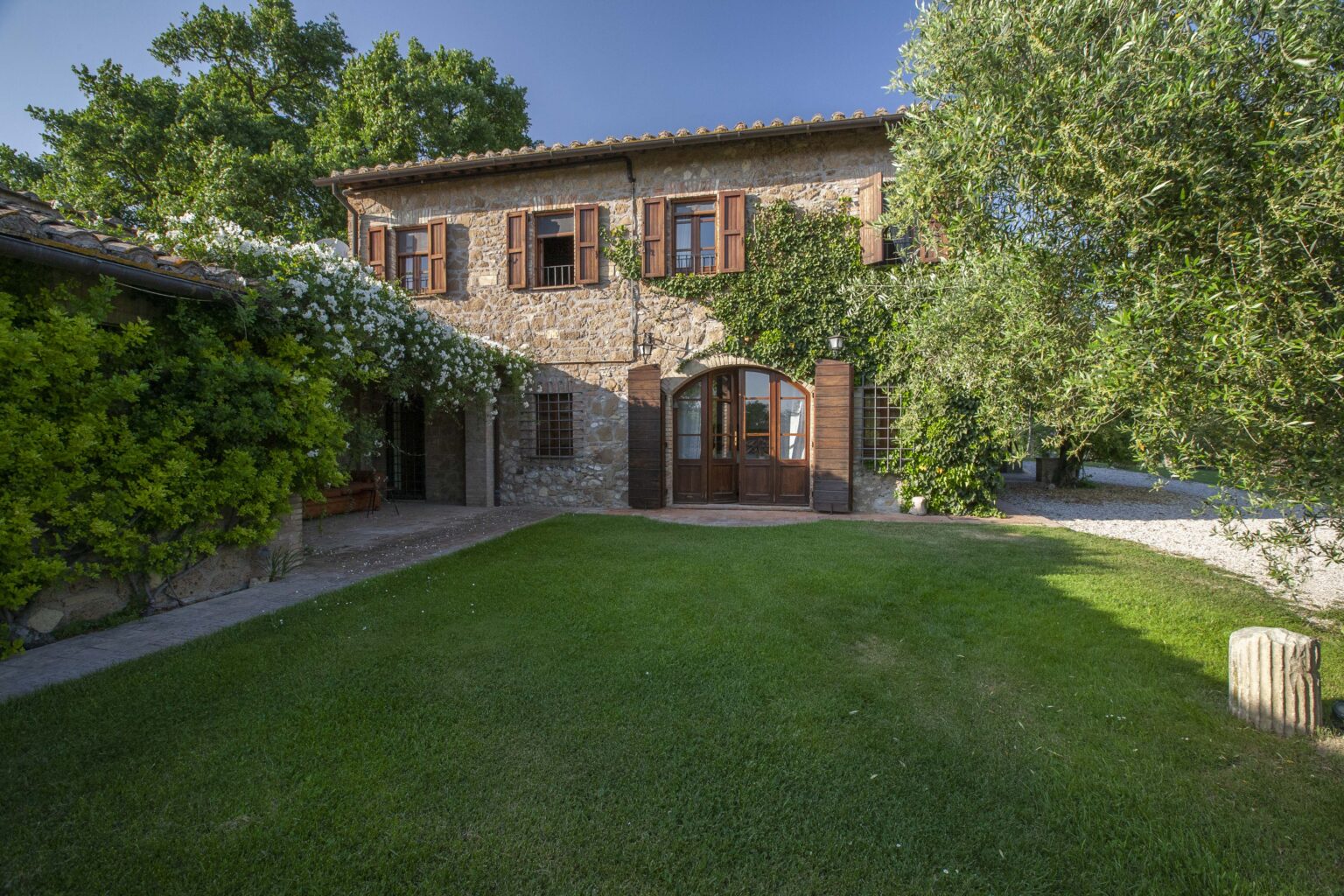 Charming stone house with wooden shutters surrounded by lush greenery and a manicured lawn, showcasing a blend of rustic architecture and natural beauty. | Only on SopranoVillas