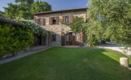 Charming stone house with wooden shutters surrounded by lush greenery and a manicured lawn, showcasing a blend of rustic architecture and natural beauty.