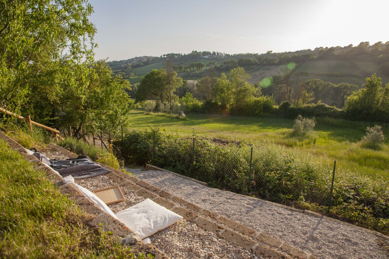 Scenic view of a lush green landscape with rolling hills under a clear sky, featuring a pathway lined with natural materials and surrounded by trees, capturing the tranquility of rural life. | Only on SopranoVillas