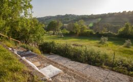 Scenic view of a lush green landscape with rolling hills under a clear sky, featuring a pathway lined with natural materials and surrounded by trees, capturing the tranquility of rural life.