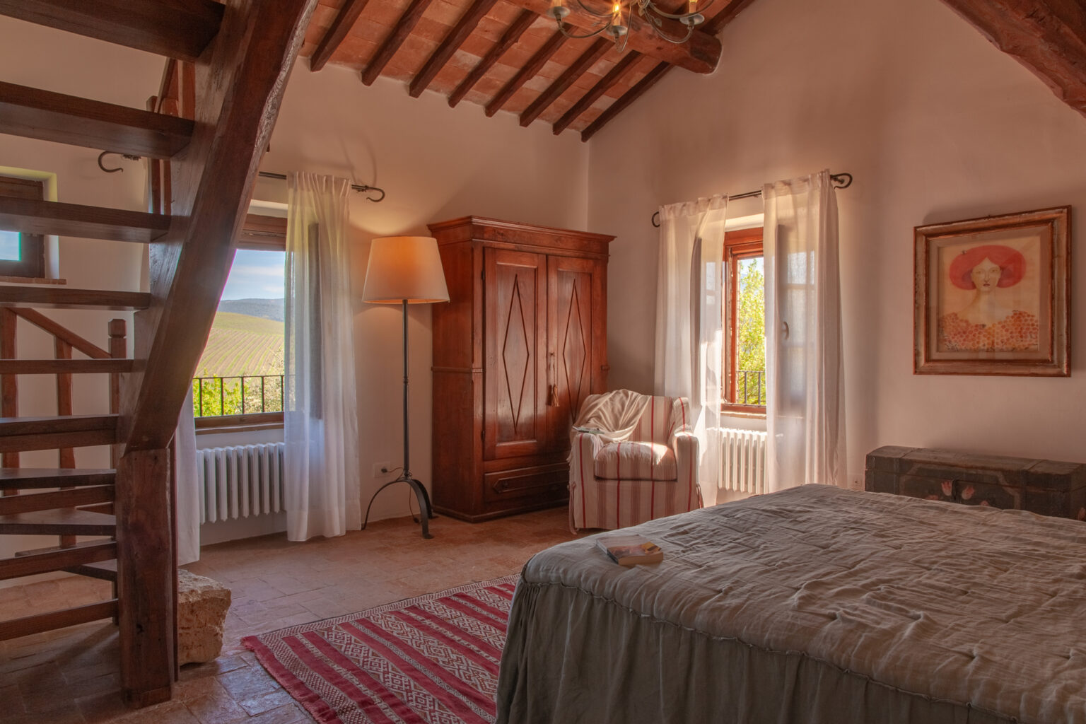 Cozy bedroom featuring rustic decor, a wooden staircase, large windows with scenic vineyard views, an antique wardrobe, and a comfortable armchair. Perfect for a relaxing getaway. | Only on SopranoVillas