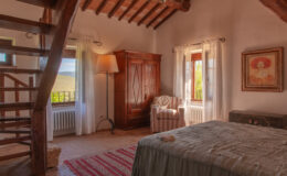 Cozy bedroom featuring rustic decor, a wooden staircase, large windows with scenic vineyard views, an antique wardrobe, and a comfortable armchair. Perfect for a relaxing getaway.
