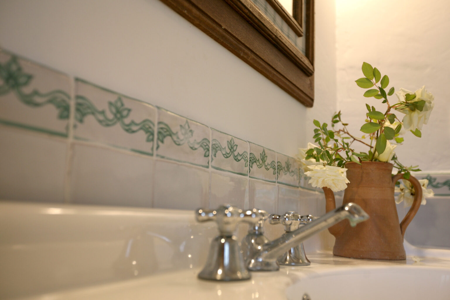 Close-up view of a bathroom sink featuring vintage-style faucets, decorative tiled backsplash, and a clay pitcher with fresh flowers, creating a charming and inviting atmosphere. | Only on SopranoVillas