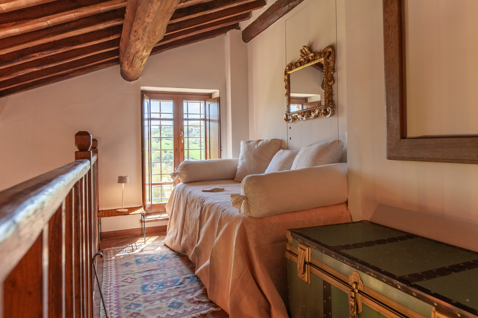 Cozy attic bedroom with wooden beams, a comfortable sofa, and a vintage mirror, featuring natural light from a window and decorative elements. | Only on SopranoVillas