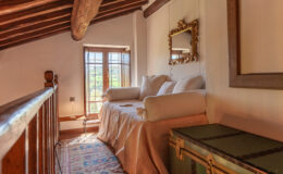 Cozy attic bedroom with wooden beams, a comfortable sofa, and a vintage mirror, featuring natural light from a window and decorative elements.