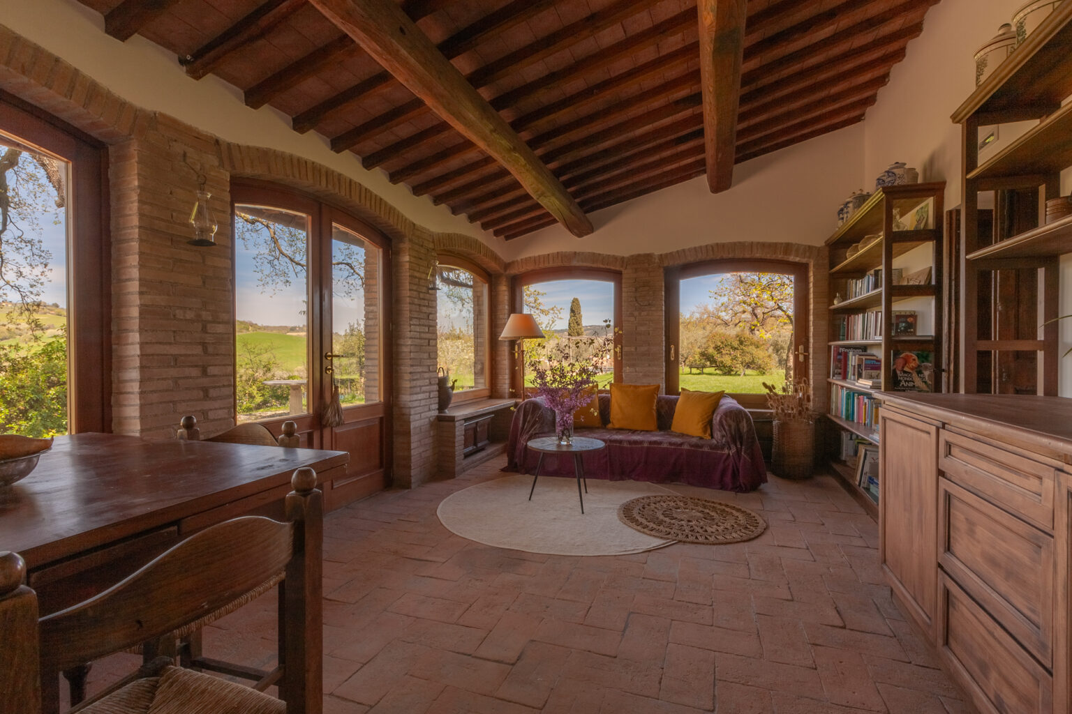 Cozy living room with large windows showcasing scenic views, rustic wooden beams, and a mix of comfortable seating and bookshelves, creating a warm and inviting atmosphere. | Only on SopranoVillas