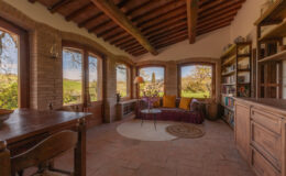 Cozy living room with large windows showcasing scenic views, rustic wooden beams, and a mix of comfortable seating and bookshelves, creating a warm and inviting atmosphere.
