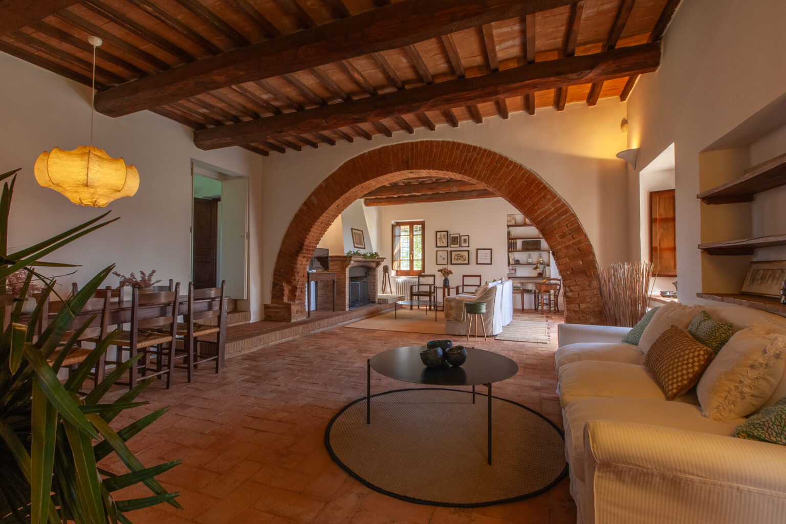 Spacious living room featuring rustic wooden beams, an arched entrance, and a cozy seating area with a coffee table. Natural light illuminates the space, showcasing a blend of modern and traditional decor. | Only on SopranoVillas