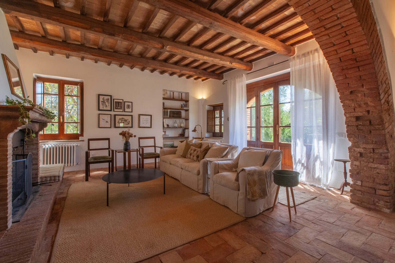 Cozy living room with wooden beams, large windows, and rustic decor, featuring a comfortable sofa, coffee table, and stylish armchair, illuminated by natural light. | Only on SopranoVillas