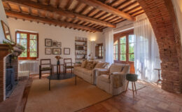 Cozy living room with wooden beams, large windows, and rustic decor, featuring a comfortable sofa, coffee table, and stylish armchair, illuminated by natural light.