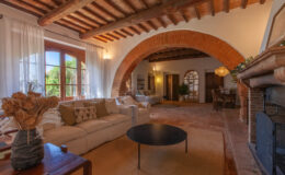 Cozy living room featuring arched ceilings, large windows with natural light, a comfortable sofa, and a stylish coffee table, creating an inviting atmosphere in a rustic home setting.