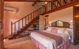 Cozy bedroom interior featuring a large bed with decorative pillows, wooden accents, and a staircase leading to an upper loft area, designed for comfort and relaxation.