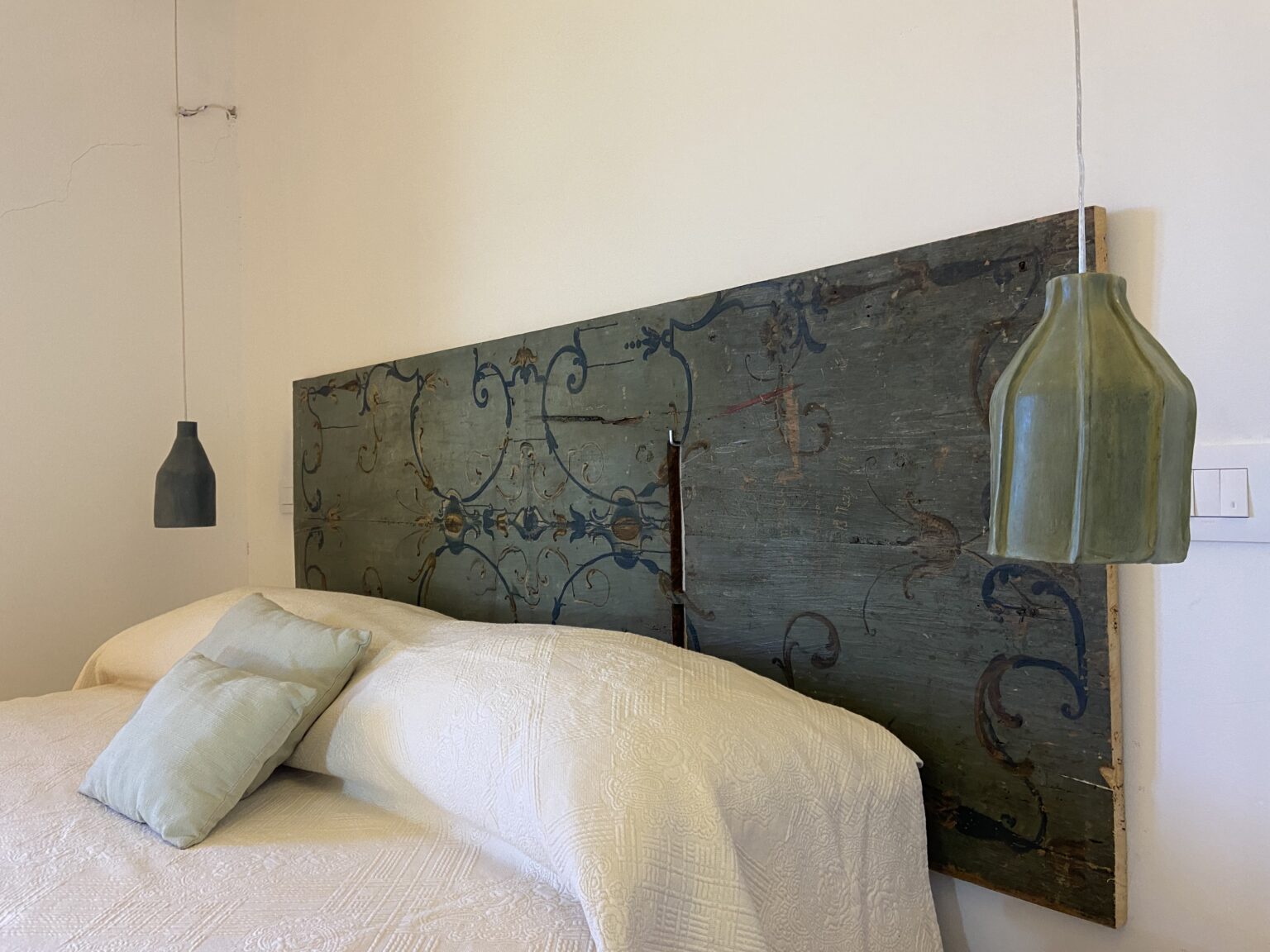 Stylish bedroom featuring a vintage blue headboard with intricate designs, complemented by two hanging green pendant lights and a cozy white bedding set with decorative pillows. | Only on SopranoVillas
