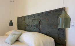 Stylish bedroom featuring a vintage blue headboard with intricate designs, complemented by two hanging green pendant lights and a cozy white bedding set with decorative pillows.