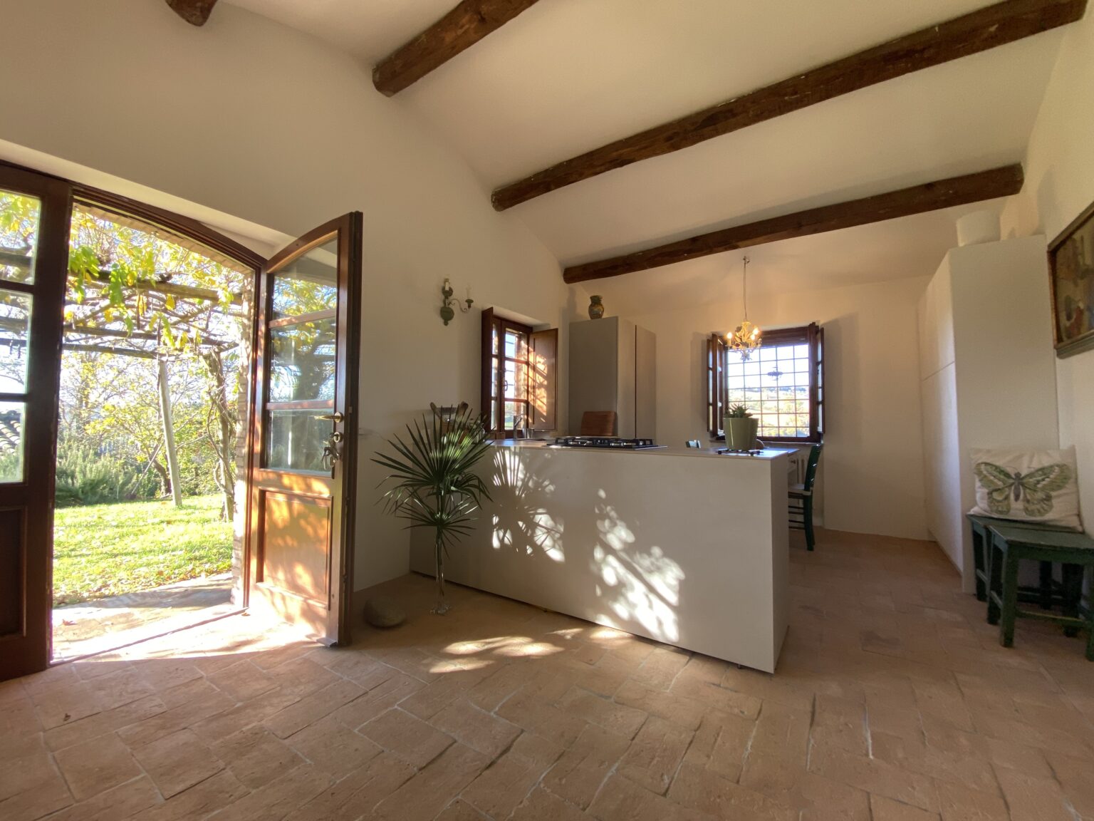 Bright and airy kitchen interior with wooden beams, featuring an open door leading to a garden view, modern white cabinetry, and natural light illuminating the space. | Only on SopranoVillas