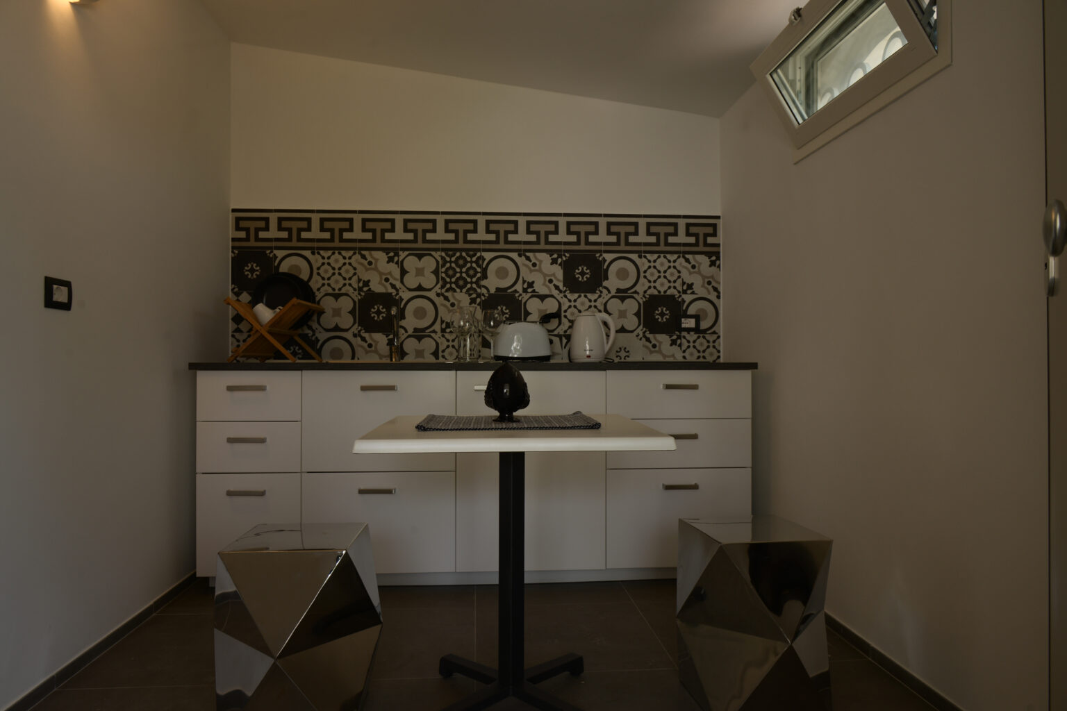 Modern kitchen interior featuring a minimalist design with white cabinetry, a stylish patterned backsplash, and a sleek table with metallic stools. | Only on SopranoVillas