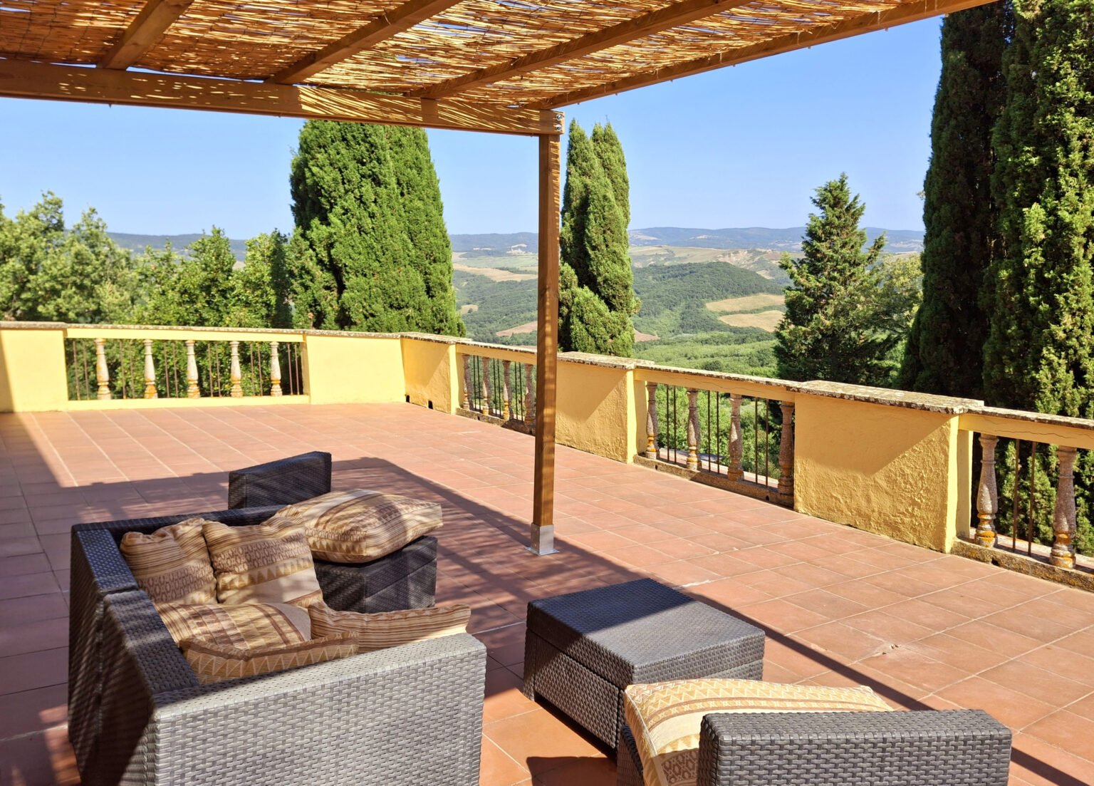 Spacious outdoor terrace with a wicker seating area, overlooking lush green hills and trees under a clear blue sky. Ideal for relaxation and enjoying scenic views. | Only on SopranoVillas